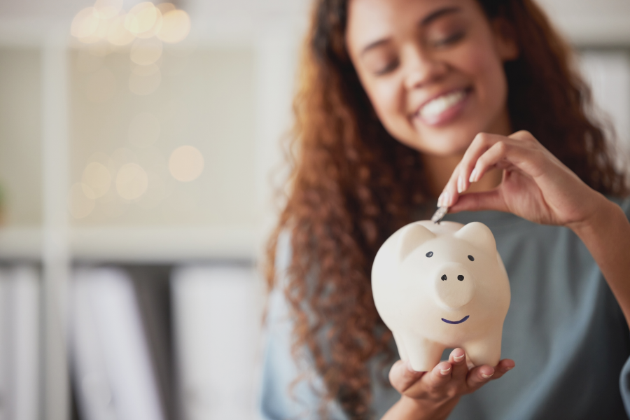 Young girl smiling while saving money in a piggy bank, symbolizing financial planning